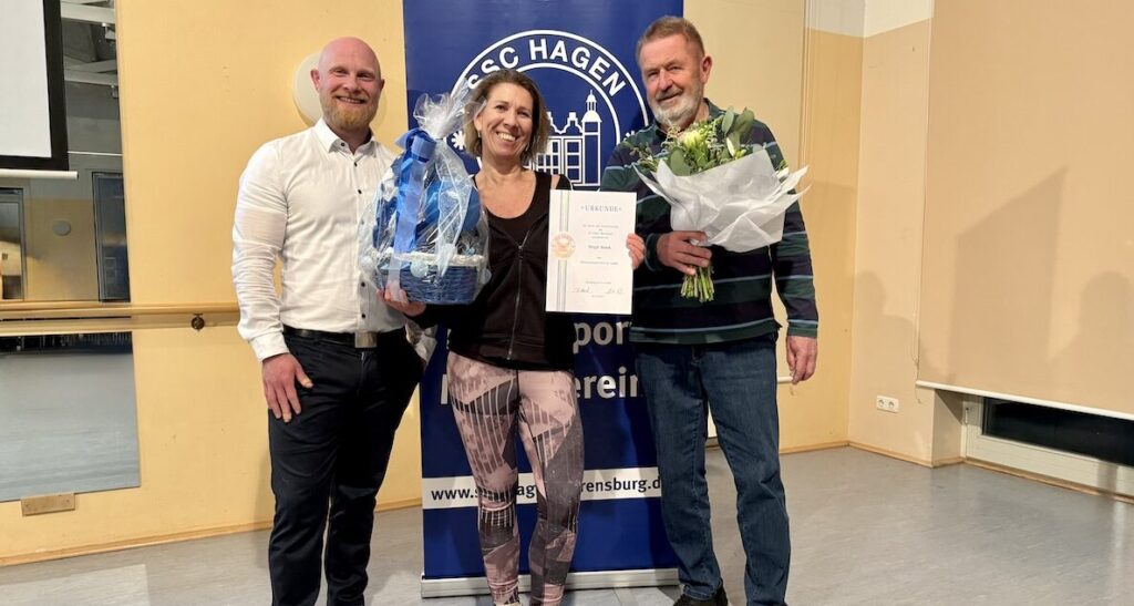 Zwei Männer und eine Frau mit Blumen und einem Geschenkkorb vor dem Banner des SSC Hagen Ahrensburg
