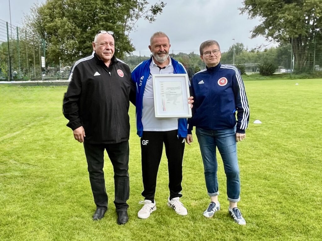 Zwei Männer und eine Frau auf einem Fußballplatz. Ehrung für Günter Feigl vom SSC Hagen Ahrensburg