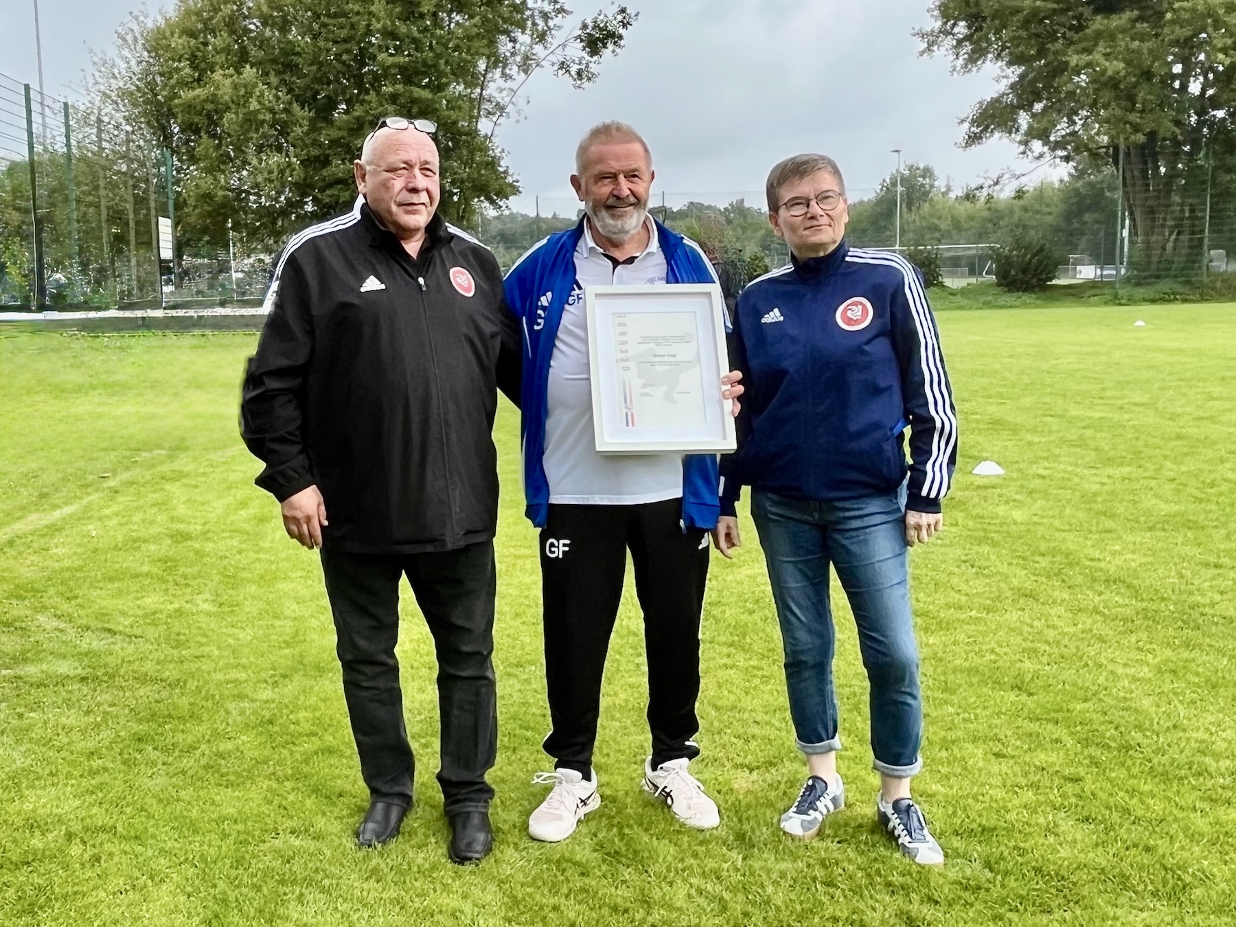 Zwei Männer und eine Frau auf einem Fußballplatz. Ehrung für Günter Feigl vom SSC Hagen Ahrensburg