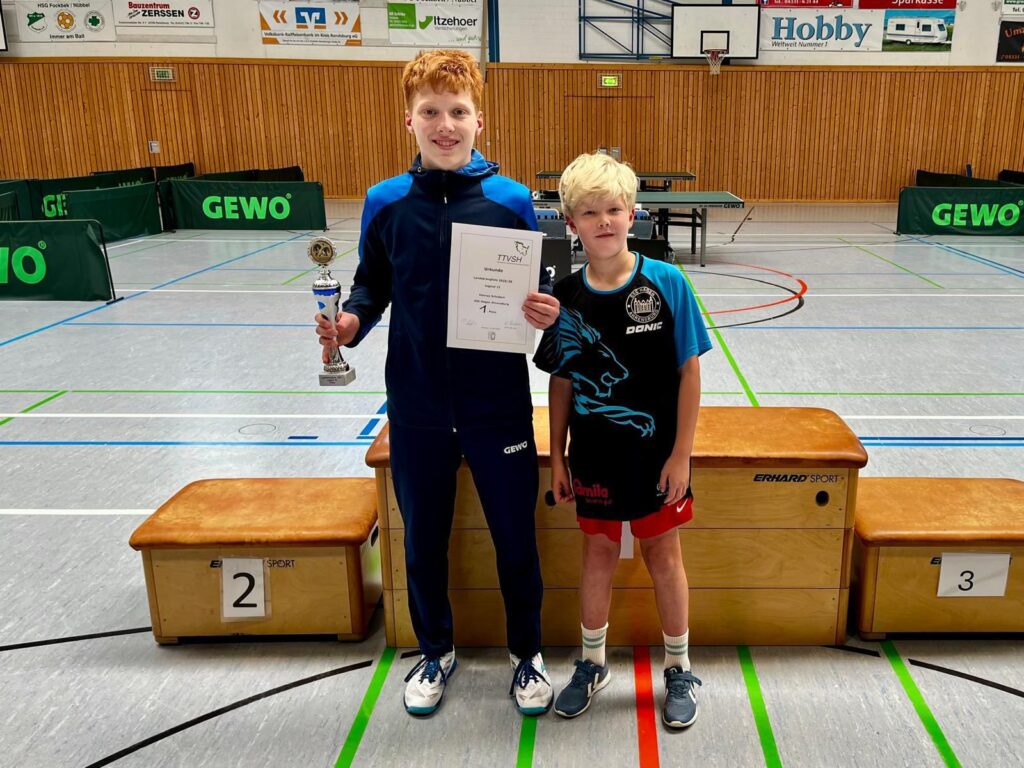 Zwei junge Tischtennisspieler vor einem Siegerpodest. Links: Hannes Schubert mit Pokal und Urkunde, rechts Piet Willemsen – Foto: Imke Willemsen