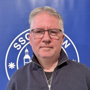 Ein Mann mit Brille vor dem Vereinslogo des SSC Hagen Ahrensburg